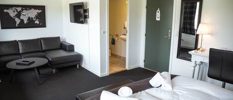 Une chambre d’hôtel avec un lit, un canapé, une petite table, une carte du monde accrochée au mur et une salle de bain visible à travers une porte ouverte.