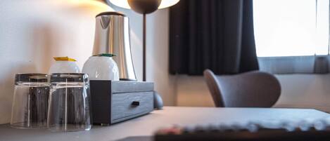 Habitación de hotel ordenada con una mesita de noche, una lámpara, un control remoto y un pequeño mueble con cajones.