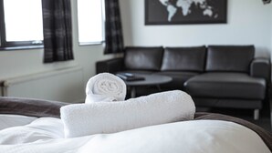 A neatly made bed with a rolled white towel, a dark leather sofa, a round coffee table, and a world map on the wall. - Hotel Runavik (Runavik)