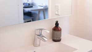 A bathroom with a white sink, a mirror, and a bottle of hand soap. - Hotel Runavik (Runavik)