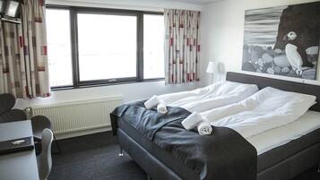 Habitación de hotel con cama, escritorio, silla, radiador y ventana con cortinas.
