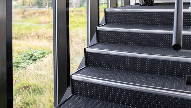 A staircase with a potted plant, large windows, and a view of a residential area. - Hotel Runavik (Runavik)