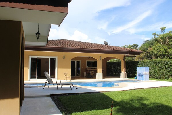Una casa con piscina, un patio techado y un césped cuidado.