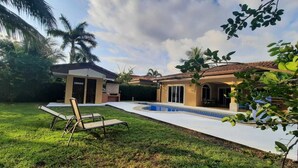 Um quintal com piscina, espreguiçadeira e um pequeno edifício com porta e janelas.