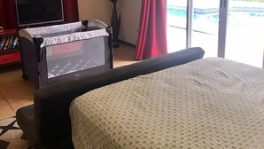 Quarto com uma cama grande, televisão, escrivaninha e vista para uma piscina.