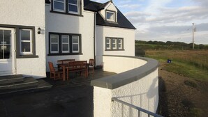 A two-story house with a white exterior and dark roof. There is a patio with a table and chairs, and a small garden area with a fence. - 4 bedroom accommodation in Portpatrick, near Stranraer (Portpatrick, near Stranraer)