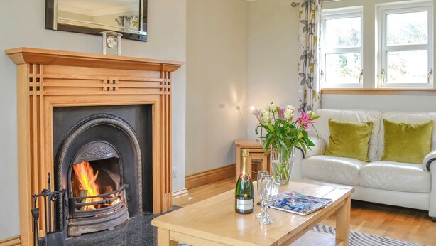 A cozy living room with a fireplace, a wooden coffee table with drinks, a white sofa, and a patterned rug. - 4 bedroom accommodation in Portpatrick, near Stranraer (Portpatrick, near Stranraer)
