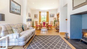 A living room with a sofa, a dining table with chairs, a fireplace, and a patterned rug.