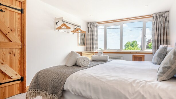 A bedroom with a large bed, a wooden wardrobe, a dresser, a mirror, and a window with curtains.