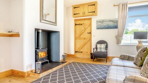 A cozy living room with a fireplace, a wooden door, a patterned rug, and a sofa with pillows.