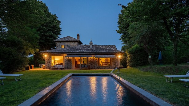 Una casa de piedra con piscina, rodeada de árboles y una terraza.