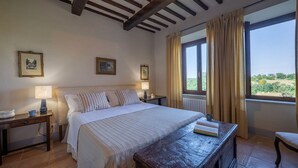 Un dormitorio con cama, mesitas de noche, una lámpara, un banco de madera y vistas al exterior.