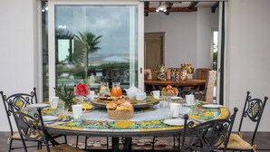 A round dining table with a colorful tablecloth, surrounded by black metal chairs with cushioned seats. - Villa Alessia 6, Emma Villas (Gela)