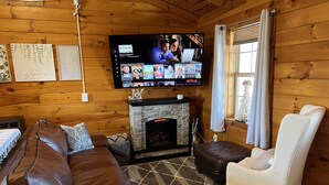 Interior acogedor de una cabaña con chimenea de piedra, sofá de cuero y televisor montado en la pared.