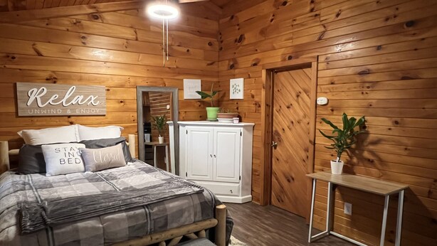 Un dormitorio acogedor de cabaña de madera con una cama, una mesita de noche, un armario y un ventilador de techo.