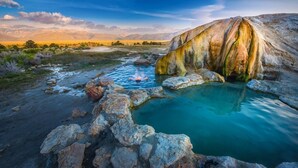 Een natuurlijke warmwaterbron, omgeven door rotsen en schaarse begroeiing.