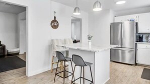 Een moderne keuken met een centraal eiland, een paar barkrukken, roestvrijstalen apparatuur, hangende lampen en een bord waarop 'yather' staat.