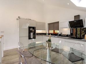 A modern kitchen with a glass dining table, a bottle of champagne, and a TV. - Waterside Lodge Five -UK38263 (Brighouse)
