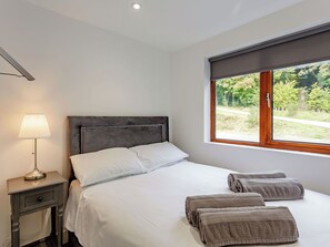 Ein Schlafzimmer mit Bett, Nachttischlampe, Fenster und Handtüchern.