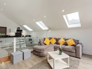 Ein moderner Wohnraum mit einem Glastisch, einer Couch mit Kissen, einem Couchtisch und einem Oberlicht.