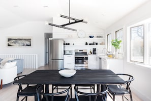 A modern kitchen with white cabinetry, a dining area with a black table and chairs, and a large window providing natural light.