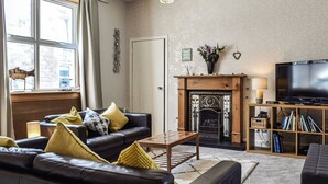 Ein Wohnzimmer mit Kamin, einer Sofagarnitur, einem Fernseher und einem Bücherregal.