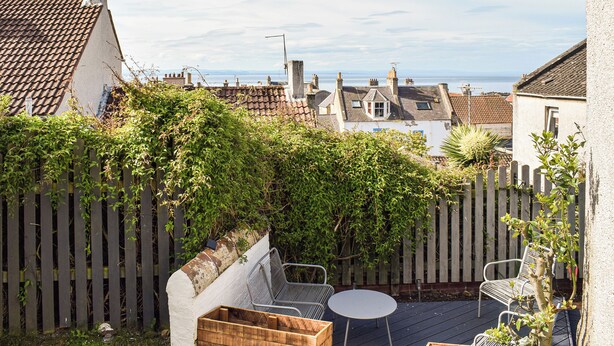 Eine Terrasse mit Tisch und Stühlen, umgeben von einem Holzzaun und viel Grün.