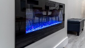 Una sala de estar moderna con un televisor de pantalla plana grande montado en la pared, piso de madera oscura y un banco tapizado en azul.