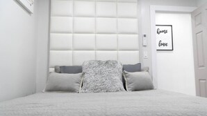 Un dormitorio con cabecera capitonada, cama con colcha texturizada gris y dos almohadas grises.