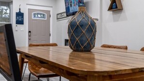 Un salón de conferencias con una mesa de madera, sillas de cuero, un jarrón decorativo, un cartel de bienvenida y una pantalla de televisión.
