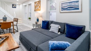 Una sala de estar moderna con un sofá gris, cojines azules, una mesa de centro de madera y una escalera que sube a otro nivel.