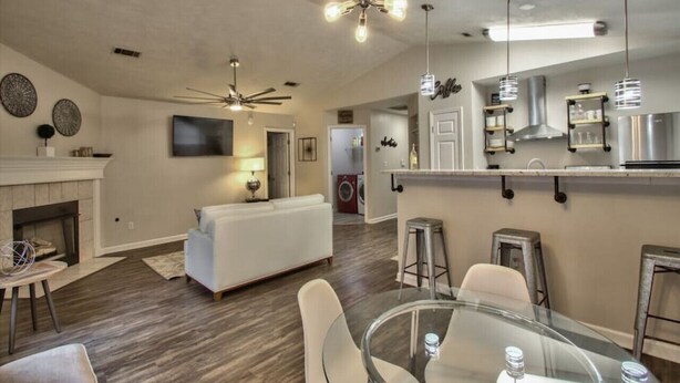 A modern living room with a fireplace, a white sofa, a glass dining table, and a kitchen area with bar stools. - Large Groups Welcome (Go Seminoles, Go Rattlers) (Tallahassee)