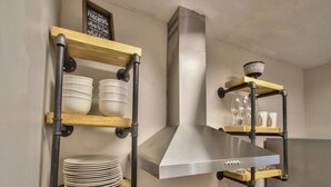 A kitchen with wooden shelves holding plates and glasses, a stainless steel range hood, and a black countertop. - Large Groups Welcome (Go Seminoles, Go Rattlers) (Tallahassee)
