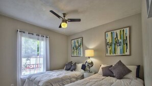 A bedroom with two beds, a ceiling fan, a window with curtains, and artwork on the walls. - Large Groups Welcome (Go Seminoles, Go Rattlers) (Tallahassee)
