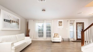 A spacious living room with a white sofa, a small white armchair, and a wooden floor. - Beautiful 2 Story Near Seaworld and Lackland AFB (San Antonio)