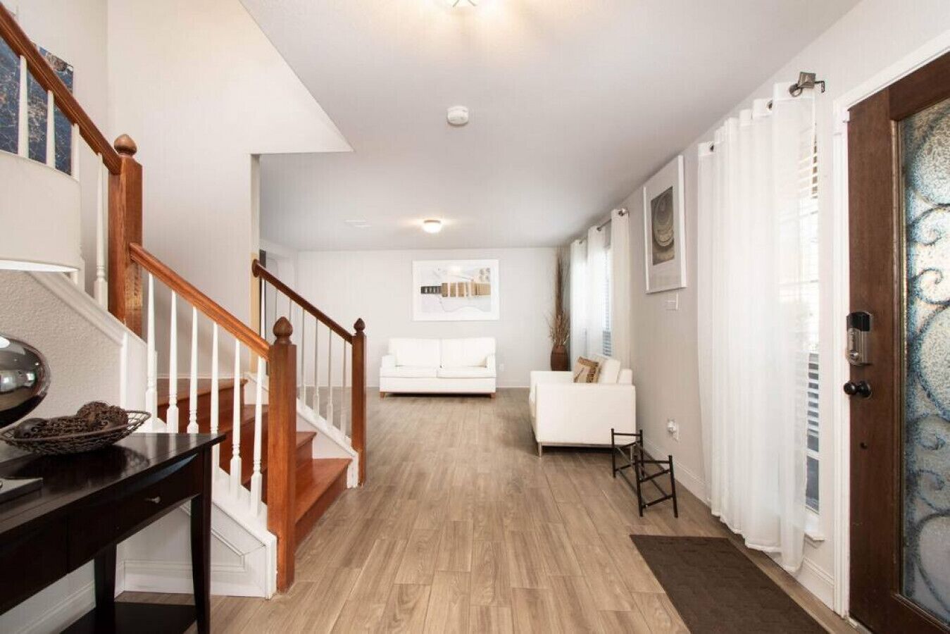 A hallway with a wooden staircase, a white sofa, and a door with a decorative glass panel.