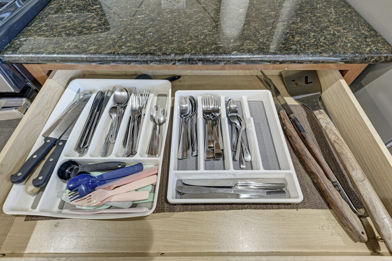 A drawer with neatly organized utensils including knives, forks, spoons, and a pair of scissors.