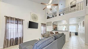 Ein geräumiges Wohnzimmer mit grauem Ecksofa, einem Flachbildfernseher und einem Deckenventilator.