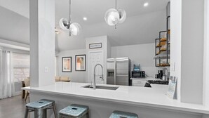 A modern kitchen with a white countertop, stainless steel appliances, and bar stools. - Newly Renovated Home near Kalahari Resorts (Round Rock)