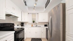 Una cocina moderna con armarios blancos, un refrigerador de acero inoxidable, una estufa negra y una encimera negra.