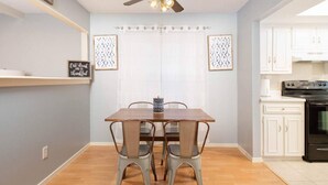 Un comedor con mesa y sillas de madera, un ventilador de techo y una cocina al fondo.