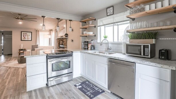 Une cuisine moderne avec des meubles blancs, des appareils en acier inoxydable et des étagères en bois.
