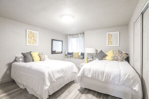 A bedroom with two beds, a window with curtains, and a wall-mounted lamp.