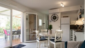A modern kitchen with white cabinets, a built-in oven, and a refrigerator. There is a dining area with a table and chairs, and a potted plant on the table.