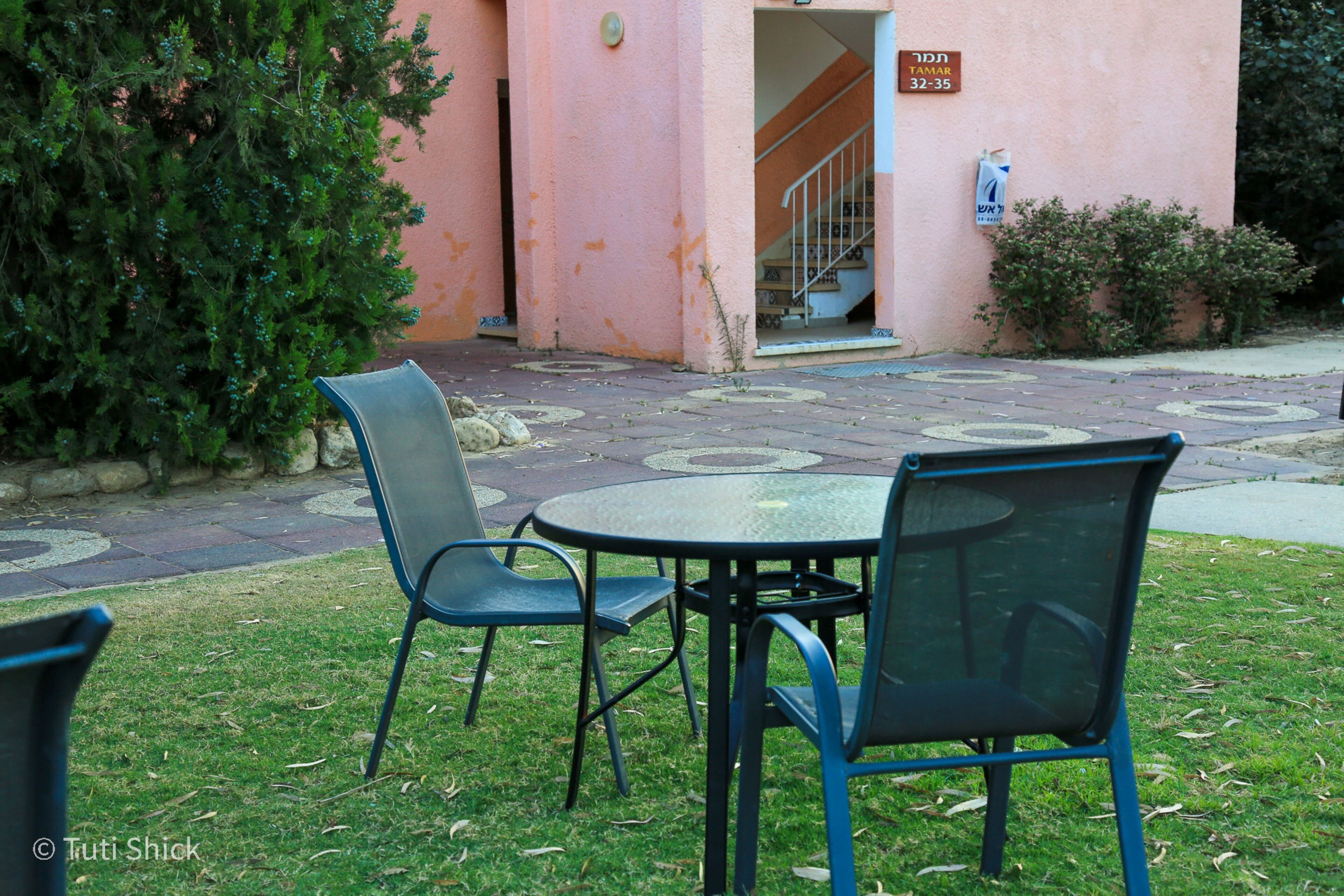 A patio area with outdoor seating, a staircase leading to an entrance, and a building with a pink facade.