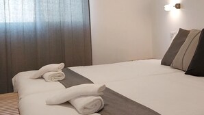 Ett hotellrum med en snyggt bäddad säng, en grå pläd och en väggmonterad lampa.