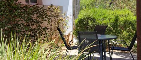 A patio with a table and chairs, surrounded by greenery and a building with a sign indicating room availability.
