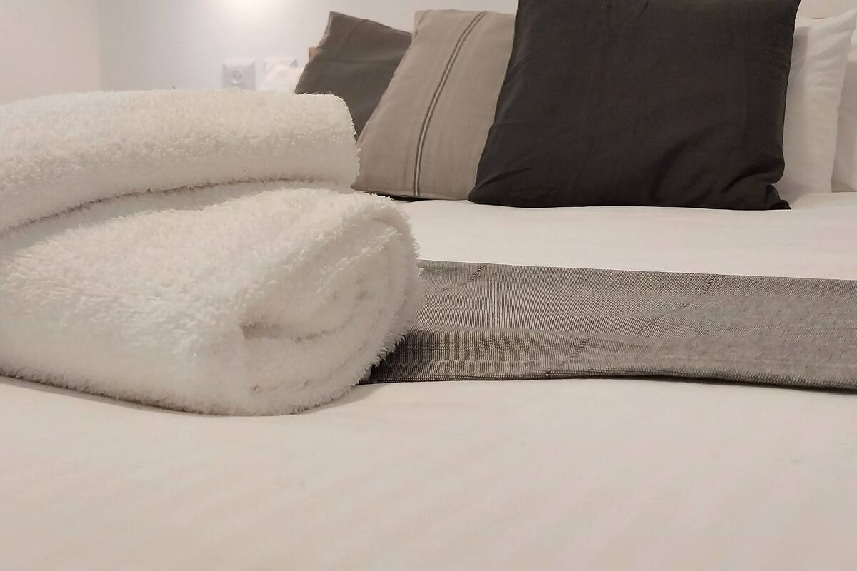 A neatly made bed with white and gray linens, a gray throw blanket, and several pillows in shades of gray and beige.