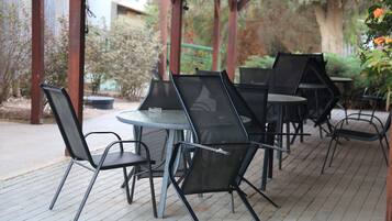 An outdoor patio with metal chairs and tables, surrounded by greenery and a wooden pergola.