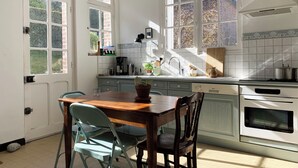 A kitchen with a wooden table, two chairs, a sink, a stove, and a window with a view of a brick building. - Seaside villa in Normandy, exceptional setting (Saint-Pierre-en-Port)
